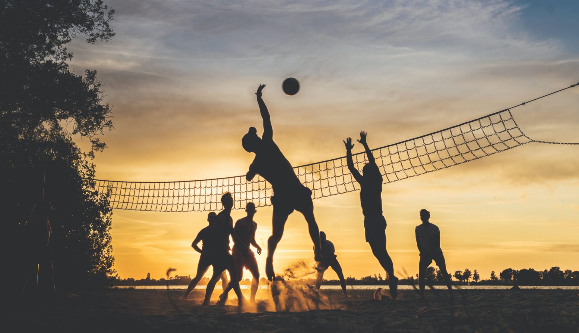 Gruppe von Menschen spielt Beachvolleyball am Strand bei Sonnenuntergang.